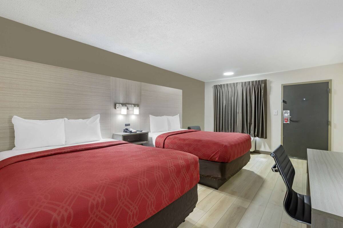 Habitación de hotel con dos camas, un escritorio, una silla, una mesita de noche y una puerta.