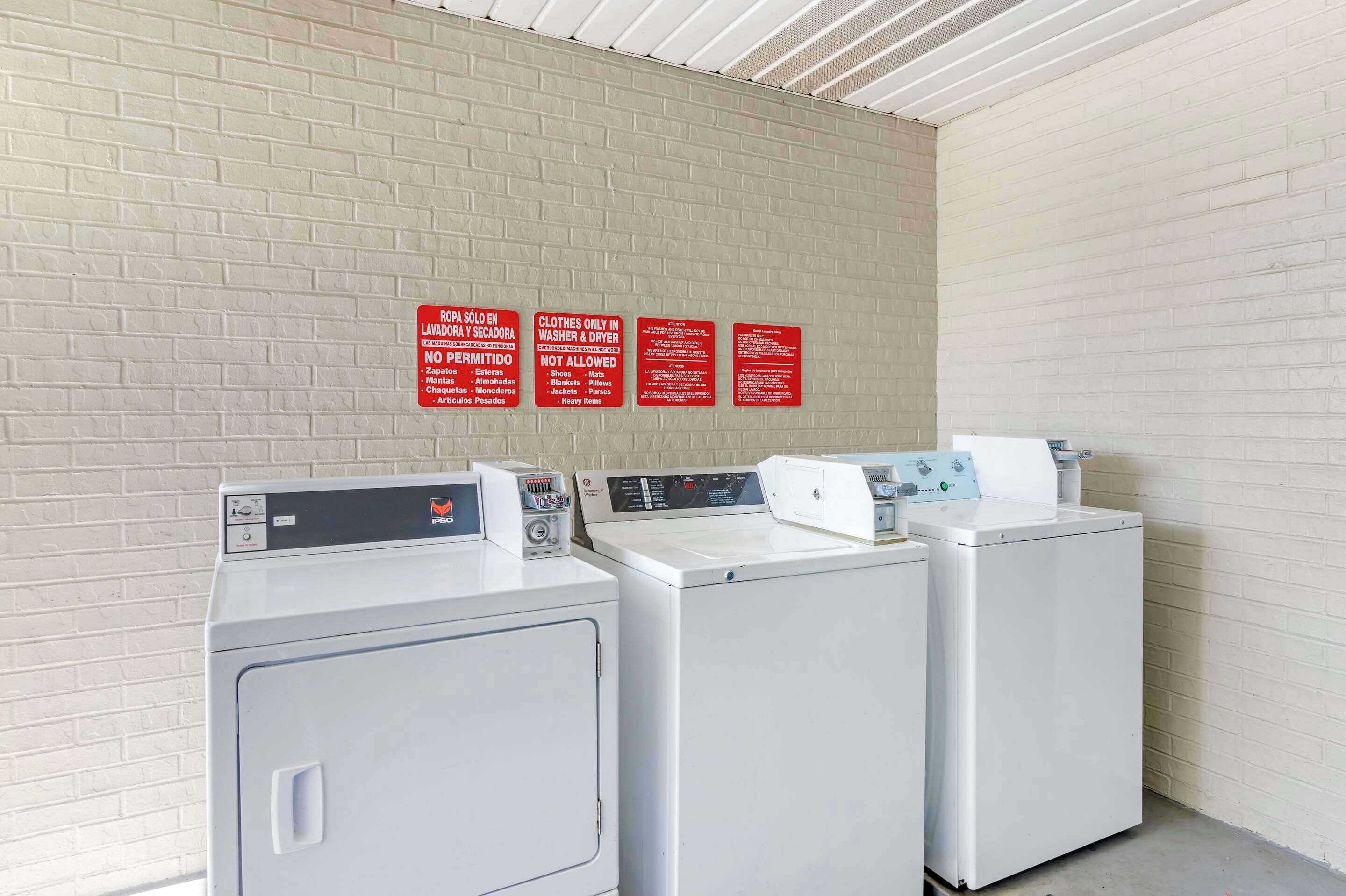 A laundry area with three washing machines and three red signs with instructions.