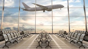 An airport terminal with rows of check-in counters and a large window offering a view of an airplane in flight.