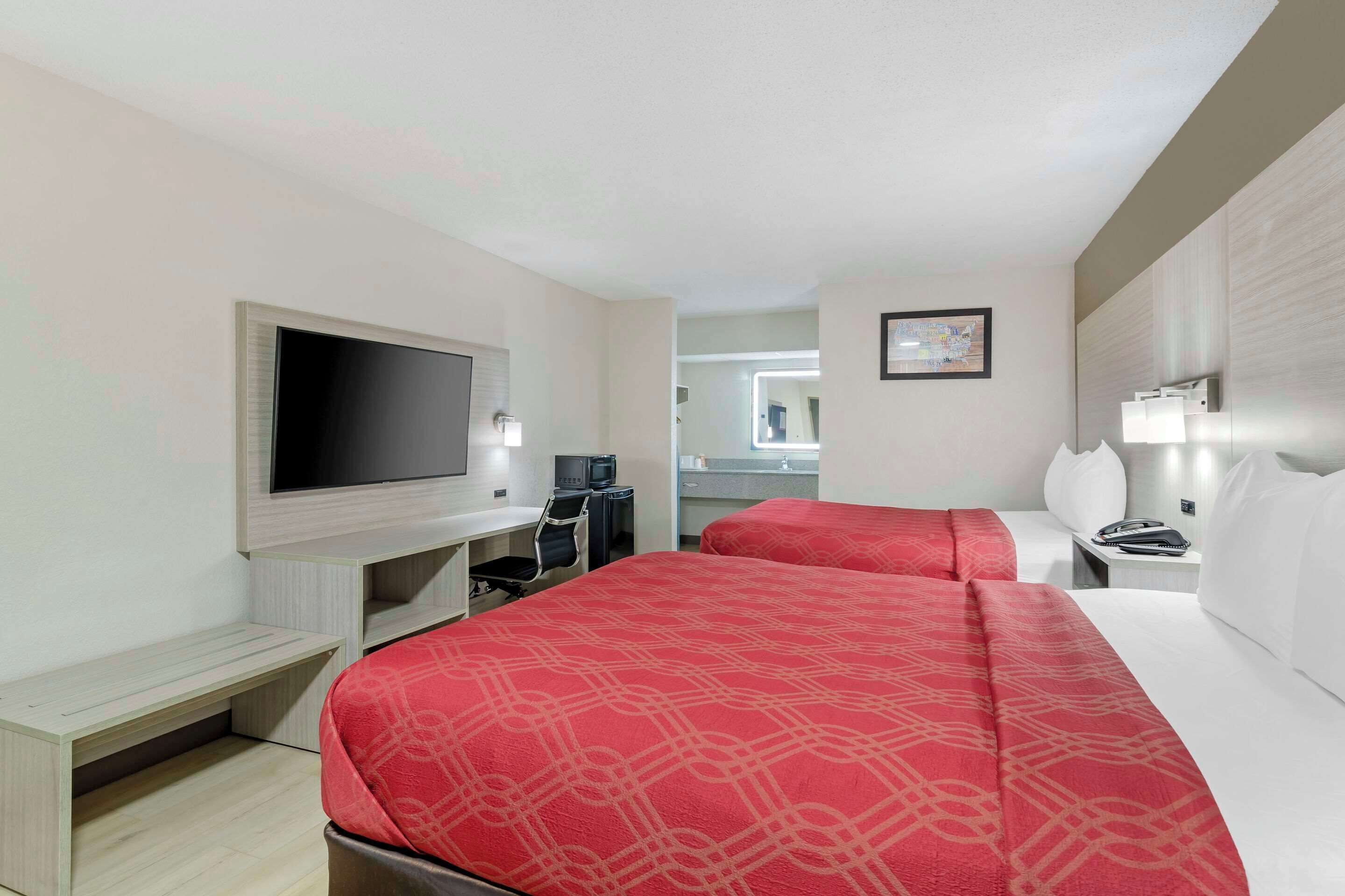 Une chambre d’hôtel avec deux lits, un bureau, une télévision et une salle de bain visible à travers une porte ouverte.