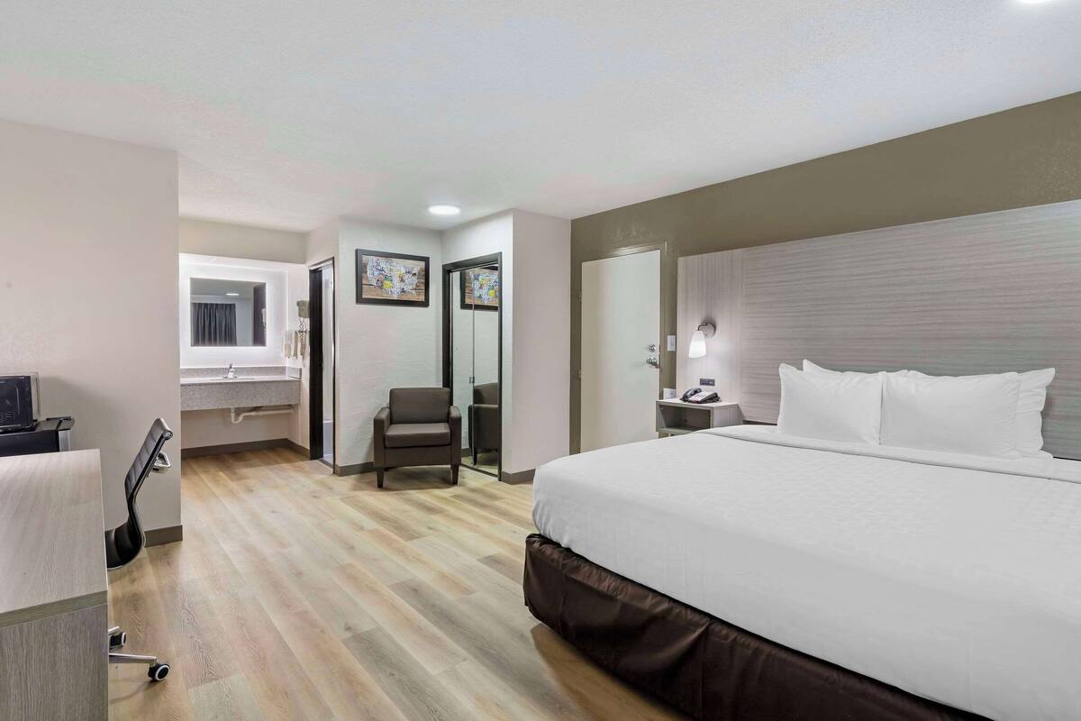 Una habitación de hotel con una cama grande, un escritorio con una silla, un tocador con espejo y una puerta que da a otra habitación.