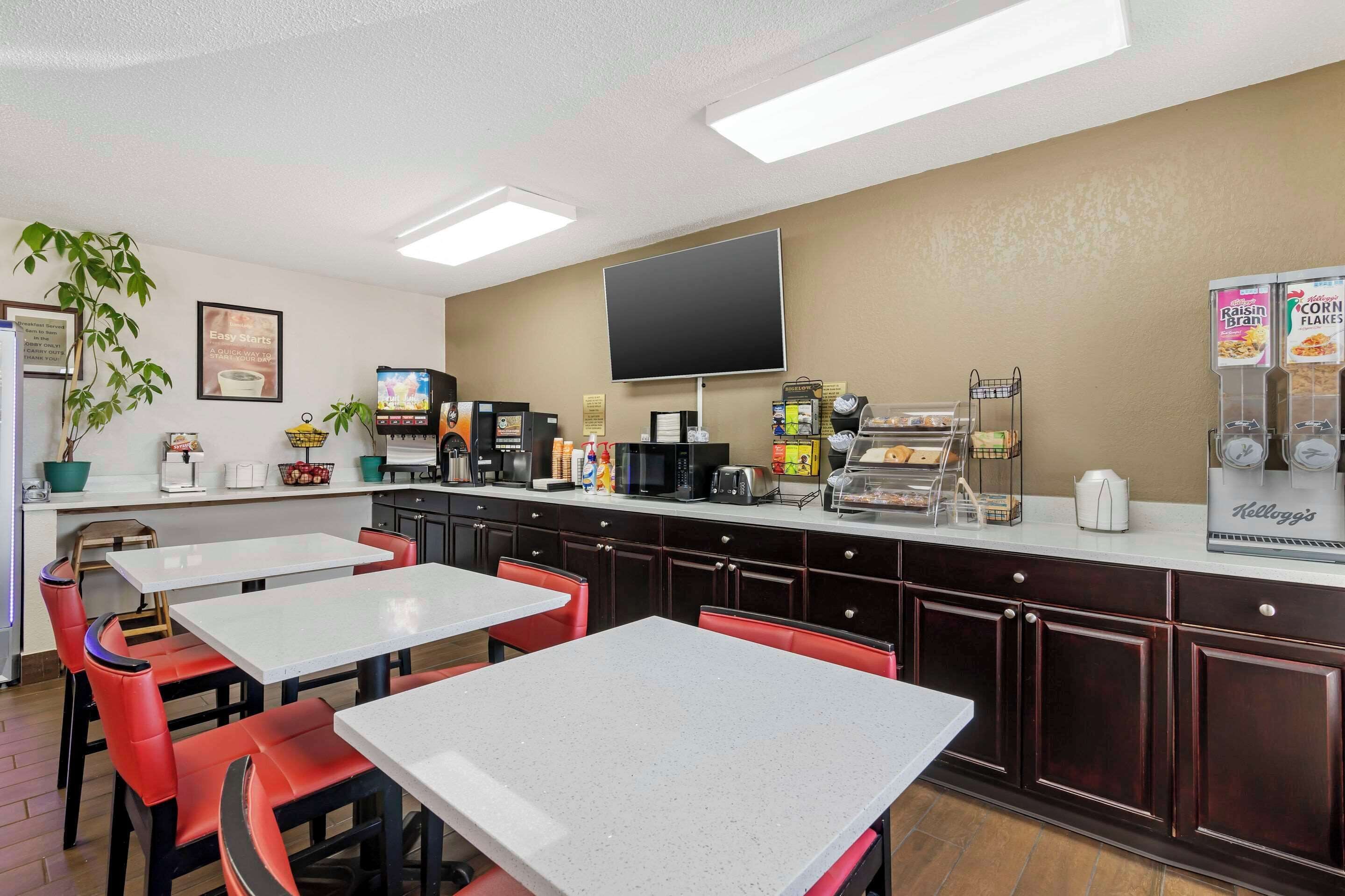 A modern kitchen area with white countertops, red chairs, and a flat-screen TV mounted on the wall.