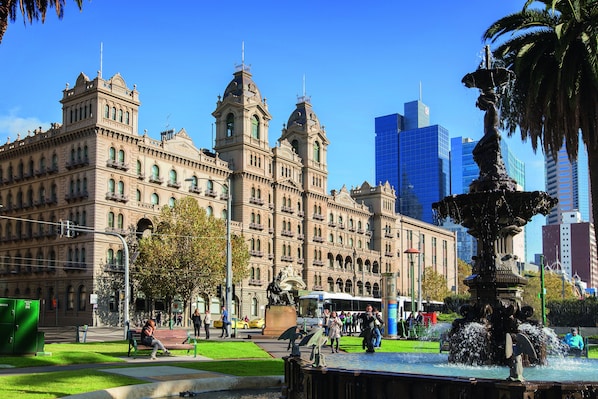 A historic building with classical architecture, a fountain, and a modern skyscraper in the background.