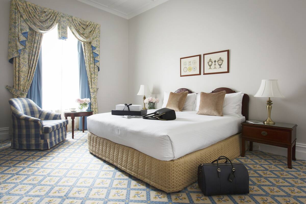 A hotel room with a large bed, a chair, a bedside table, and a lamp.
