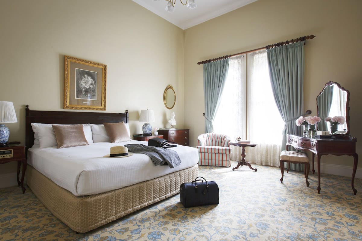 A neatly arranged bedroom with a large bed, a chair, a dresser, and a mirror.