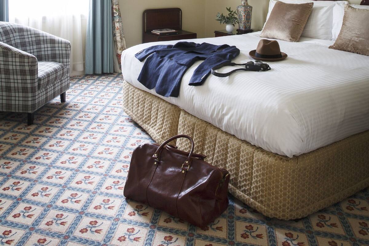 A hotel room with a large bed, a chair, a lamp, and a handbag on the floor.
