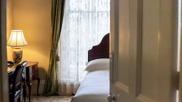 Una habitación de hotel con una cama, un escritorio con lámpara y una ventana con cortinas ligeras.