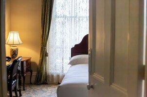 A hotel room with a bed, a desk with a lamp, and a window with sheer curtains.