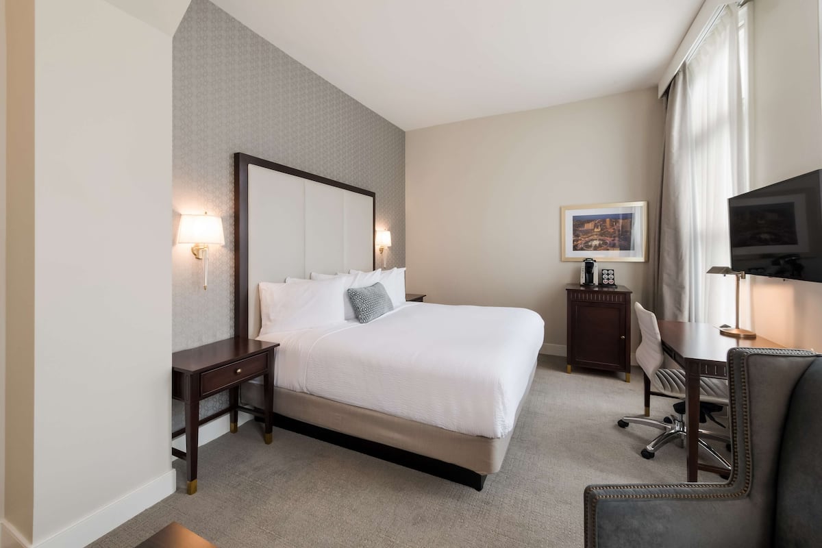 A hotel room with a large bed, bedside tables, a desk, and a chair.