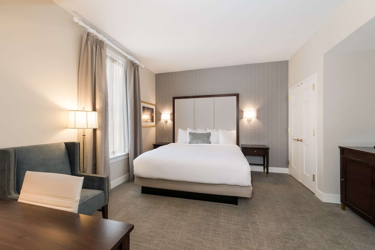 A hotel room with a large bed, a desk, a chair, a nightstand, and a lamp.
