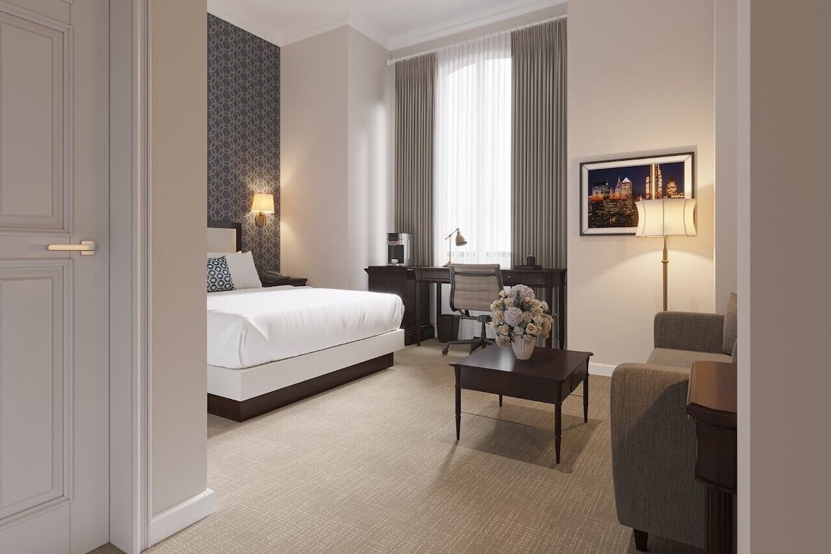 A hotel room with a bed, desk, chair, and a lamp.