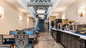 A modern hotel lobby with a central staircase, wooden flooring, and a mix of seating arrangements including tables and chairs.