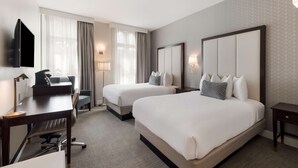 A hotel room with two beds, a desk with a chair, a TV, and a lamp.