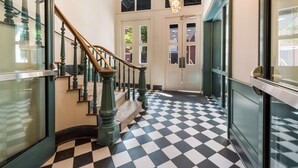 A hallway with a checkered floor, a staircase with wooden balusters, and a chandelier.