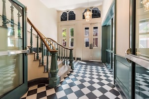 A hallway with a checkered floor, a staircase with wooden balusters, and a chandelier.