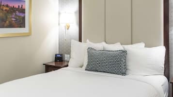 A hotel room with a neatly made bed, a bedside table with a lamp, and a framed cityscape picture on the wall.