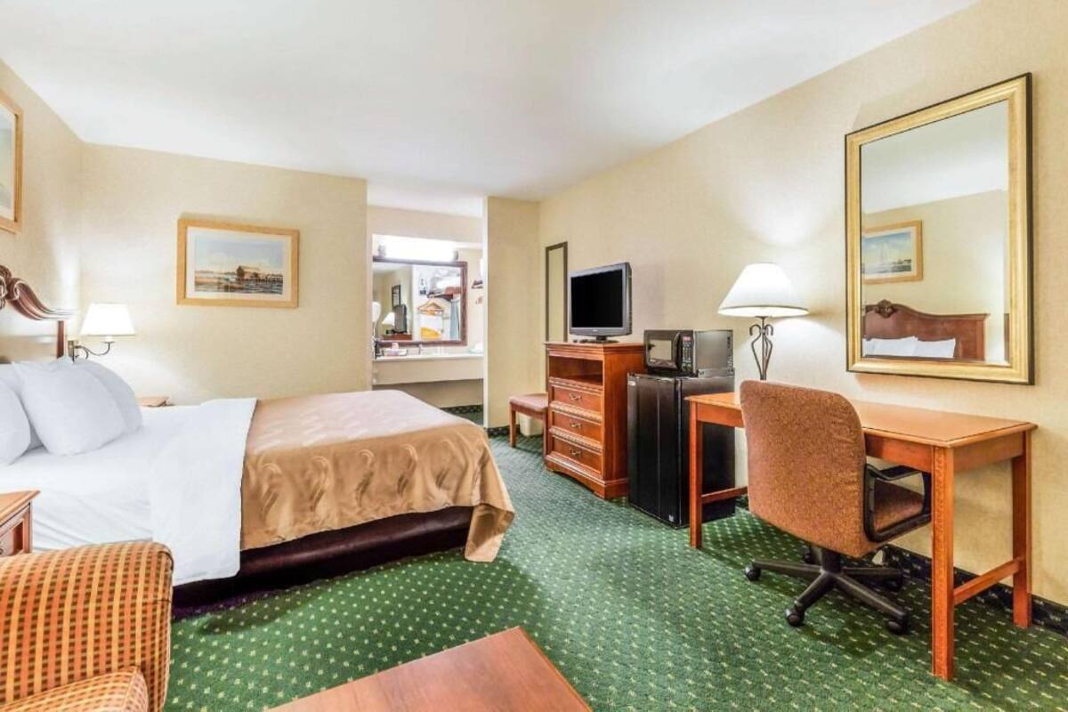 A hotel room with a bed, desk, chair, television, and a mirror.