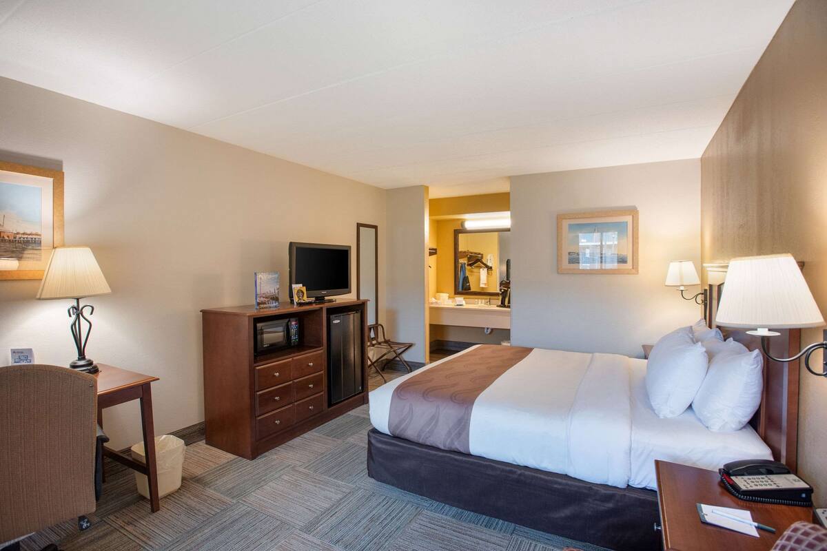 A hotel room with a bed, desk, TV, and bathroom.