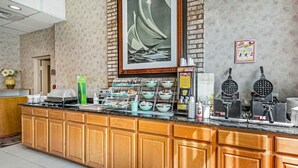 Zona de recepción de un hotel con mostrador de madera, un cuadro grande de un velero y una estación de waffles.