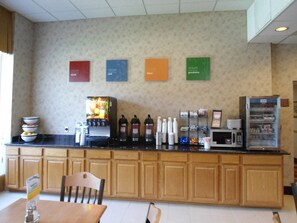 A kitchenette with a coffee machine, microwave, and various condiments. There are four signs on the wall, each with a different message.