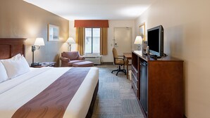 Una habitación de hotel con una cama grande, un escritorio, una silla, un televisor y una ventana con cortinas.