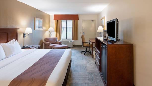 Una habitación de hotel con una cama grande, un escritorio, una silla, un televisor y una ventana con cortinas.