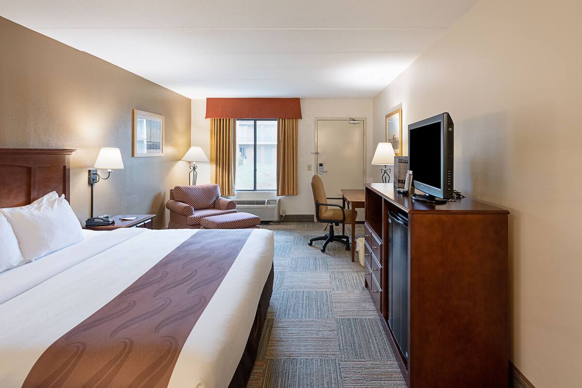 A hotel room with a large bed, a desk, a chair, a television, and a window with curtains.
