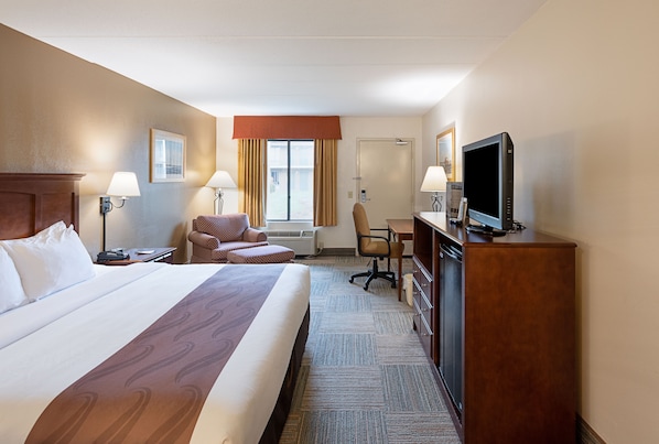 A hotel room with a large bed, a desk, a chair, a television, and a window with curtains.