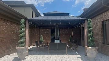 A covered outdoor seating area with brick walls, two potted plants, and a table and chairs.