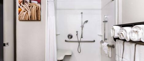 A shower with a glass door, a towel rack with folded towels, and a small shelf.