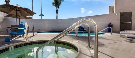 A pool area with a hot tub, lounge chairs, and a covered seating area.
