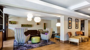 Una sala moderna con un sofá de cuero marrón, sillones a rayas y un reposapiés verde.