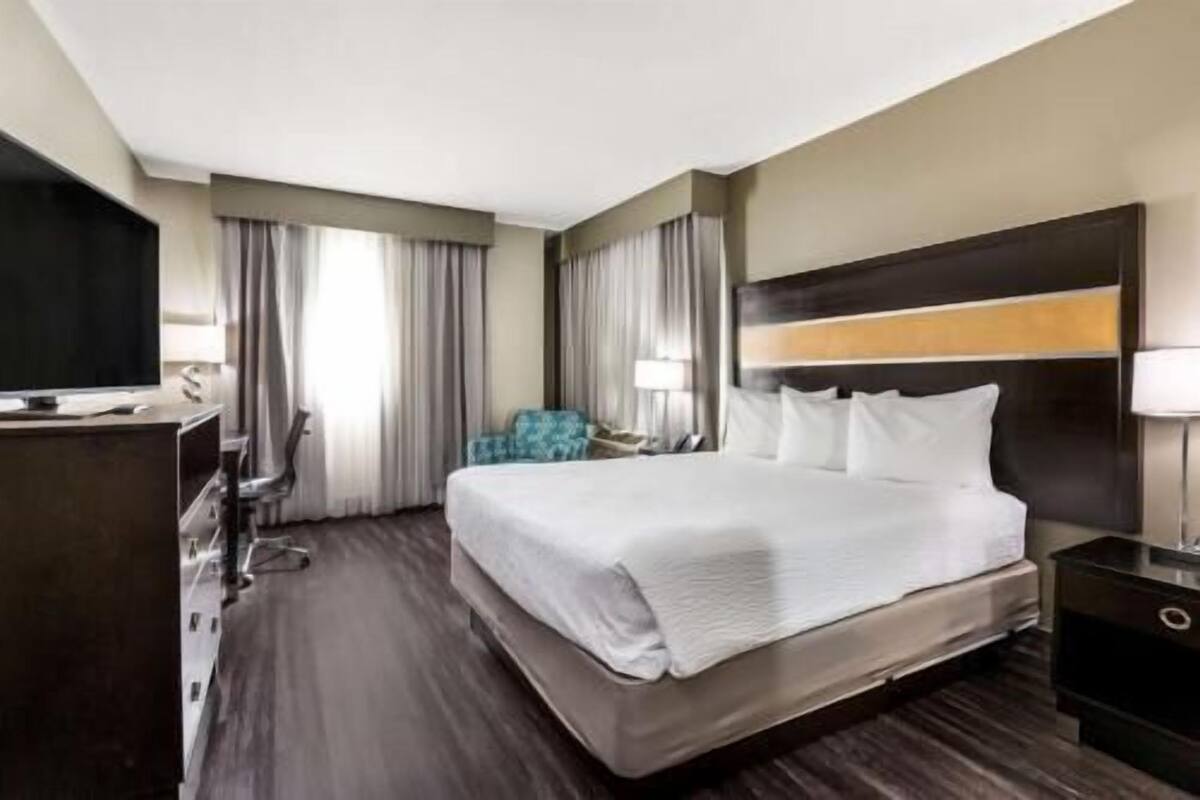 Een hotelkamer met een groot bed, een bureau met een flatscreen televisie, een stoel en een nachtkastje met een lamp.