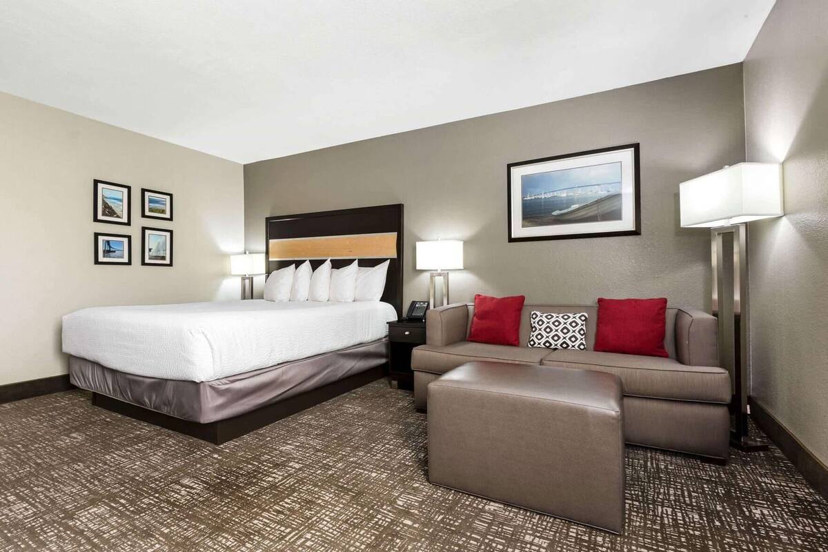 Ein Hotelzimmer mit einem Bett, einem Schlafsofa, einem kleinen Hocker, einem Nachttisch, einer Lampe und gerahmten Bildern an den Wänden.