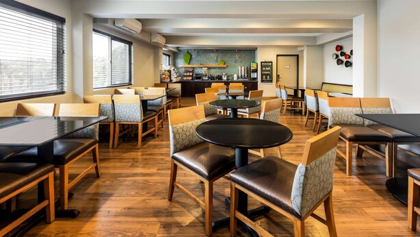 Un comedor moderno con mesas y sillas de madera, una barra central y vistas de la ciudad a través de grandes ventanales.