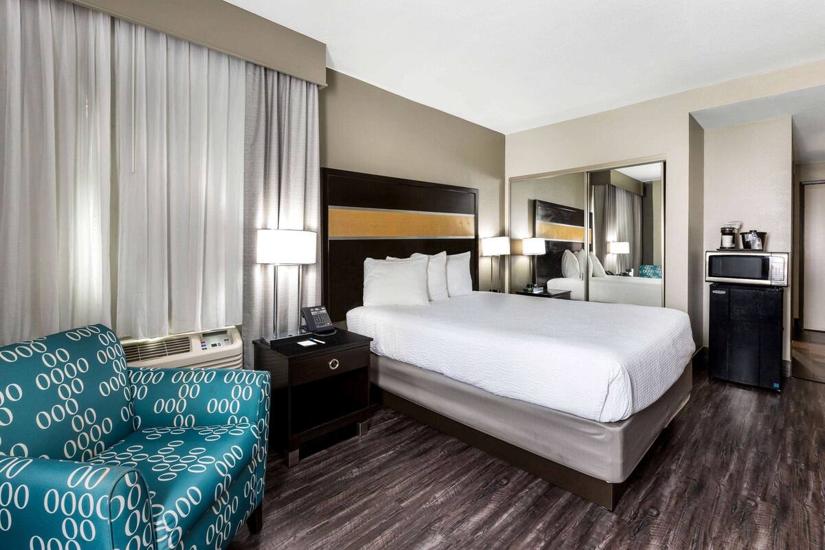 Een hotelkamer met een groot bed, een bureau met lamp, een stoel, een minibar en een spiegel.