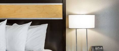 A hotel room with a bed, white pillows, a nightstand with a lamp, and a telephone.