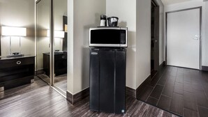 Una kitchenette compacta con microondas y cafetera, un piso de madera oscura y un espejo que refleja la habitación.