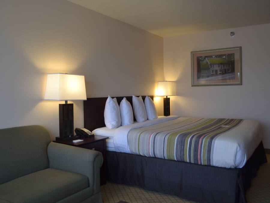 A hotel room with a bed, two bedside lamps, a chair, and a framed picture on the wall.
