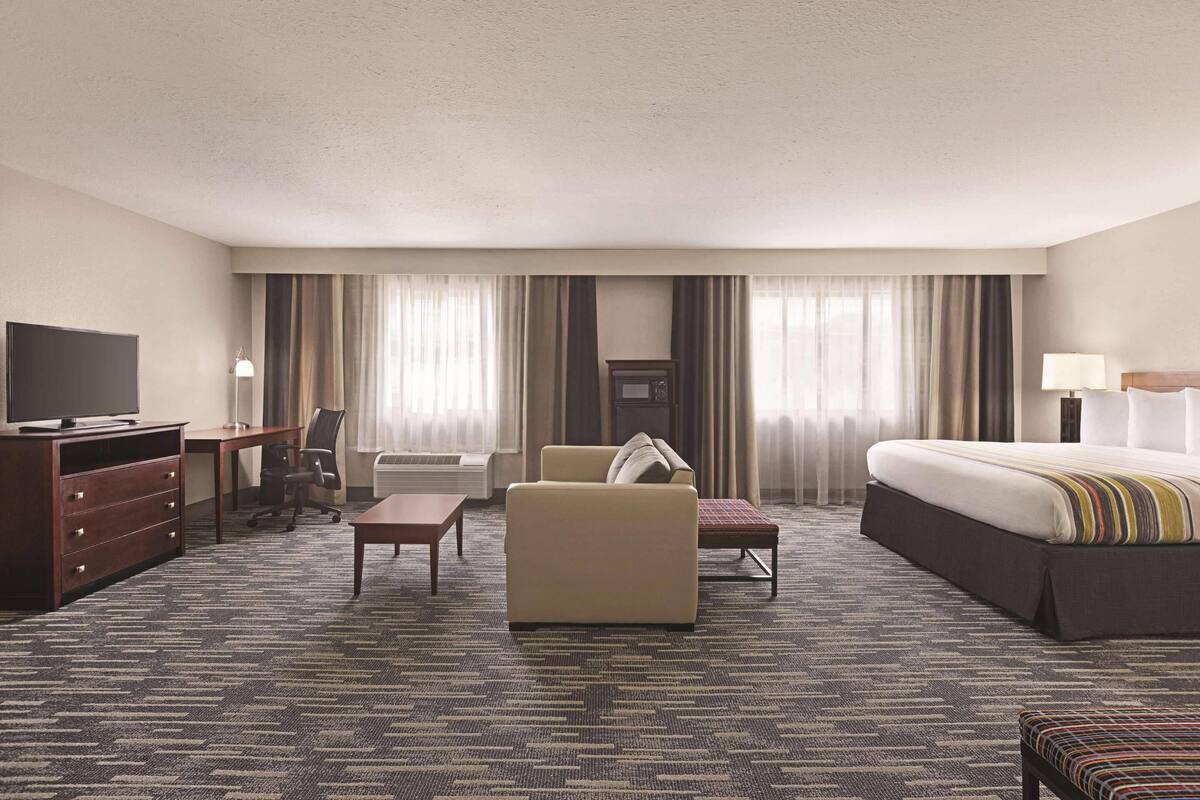 A hotel room with a large bed, a desk with a TV, a sofa, a chair, and a small table.