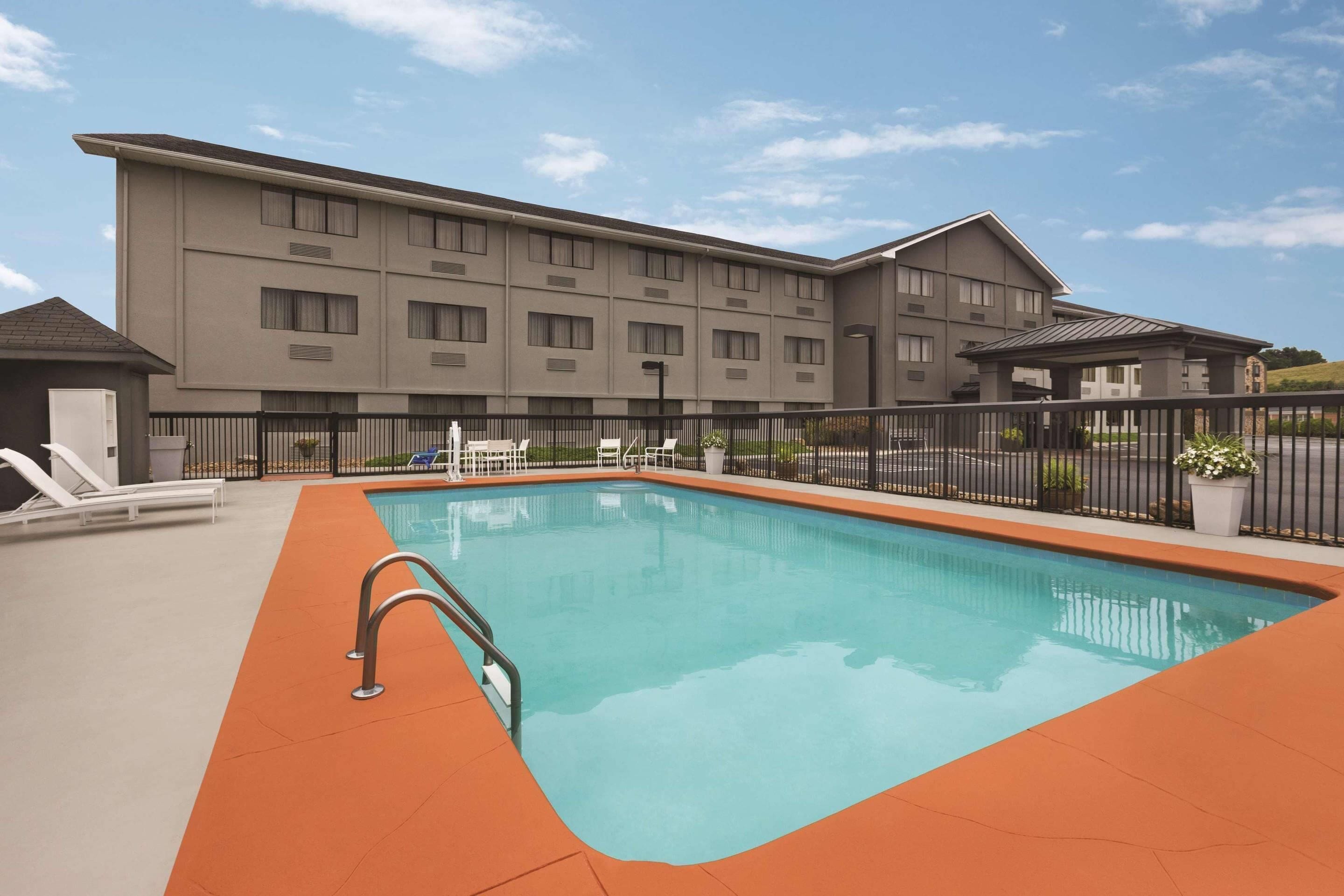 A swimming pool with a metal ladder, surrounded by a fence, and adjacent to a multi-story building with balconies.