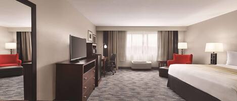 Une chambre d’hôtel avec un grand lit, un bureau avec une chaise, une télévision, une commode et un banc.