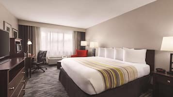 Habitación de hotel con una cama grande, un escritorio, una silla, un televisor y una ventana con cortinas.