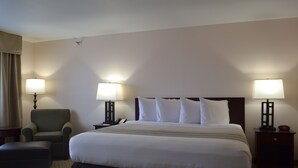 A hotel room with a large bed, two bedside tables with lamps, a chair, and a small table.
