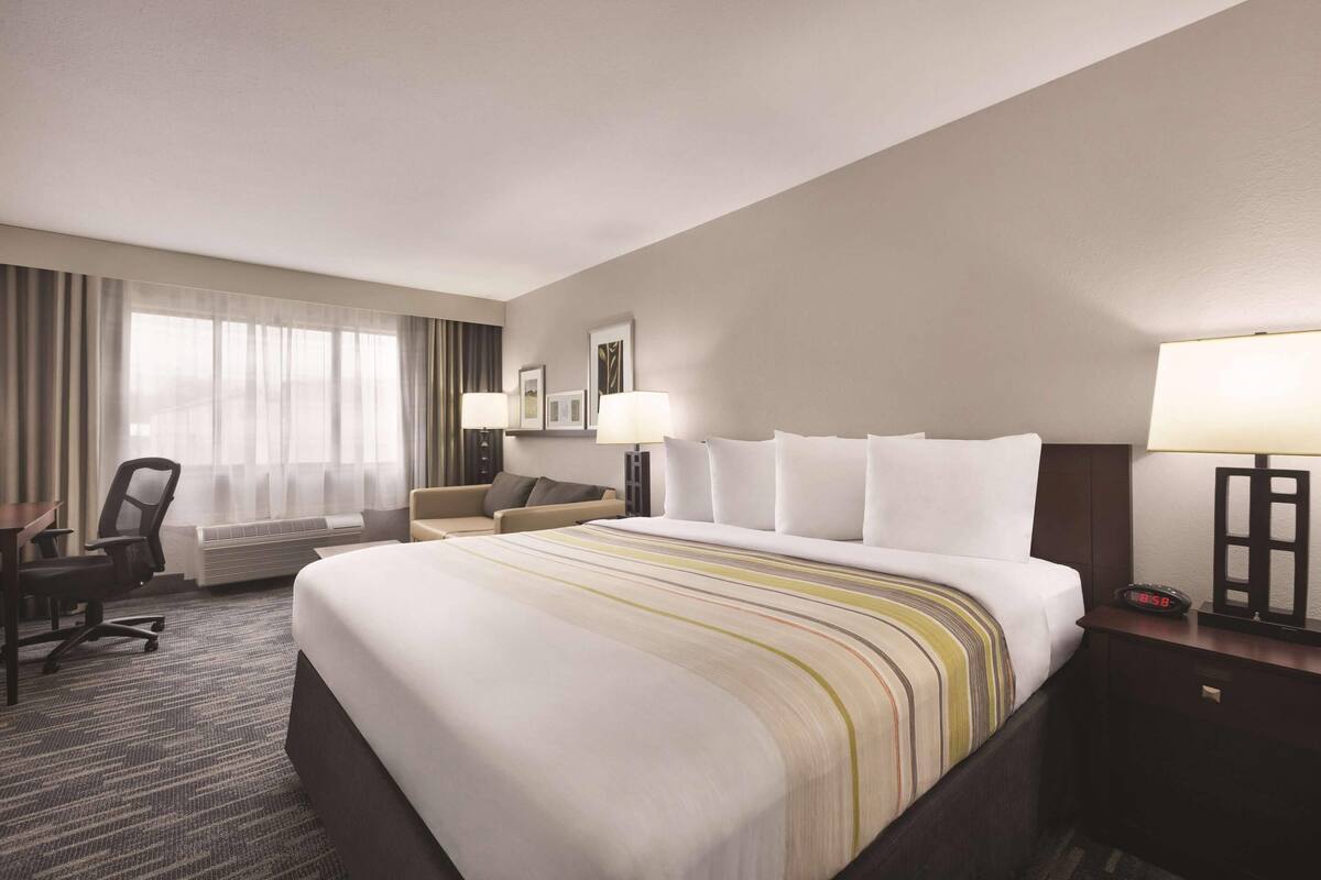 A hotel room with a large bed, a desk, a chair, a sofa, and a window with curtains.