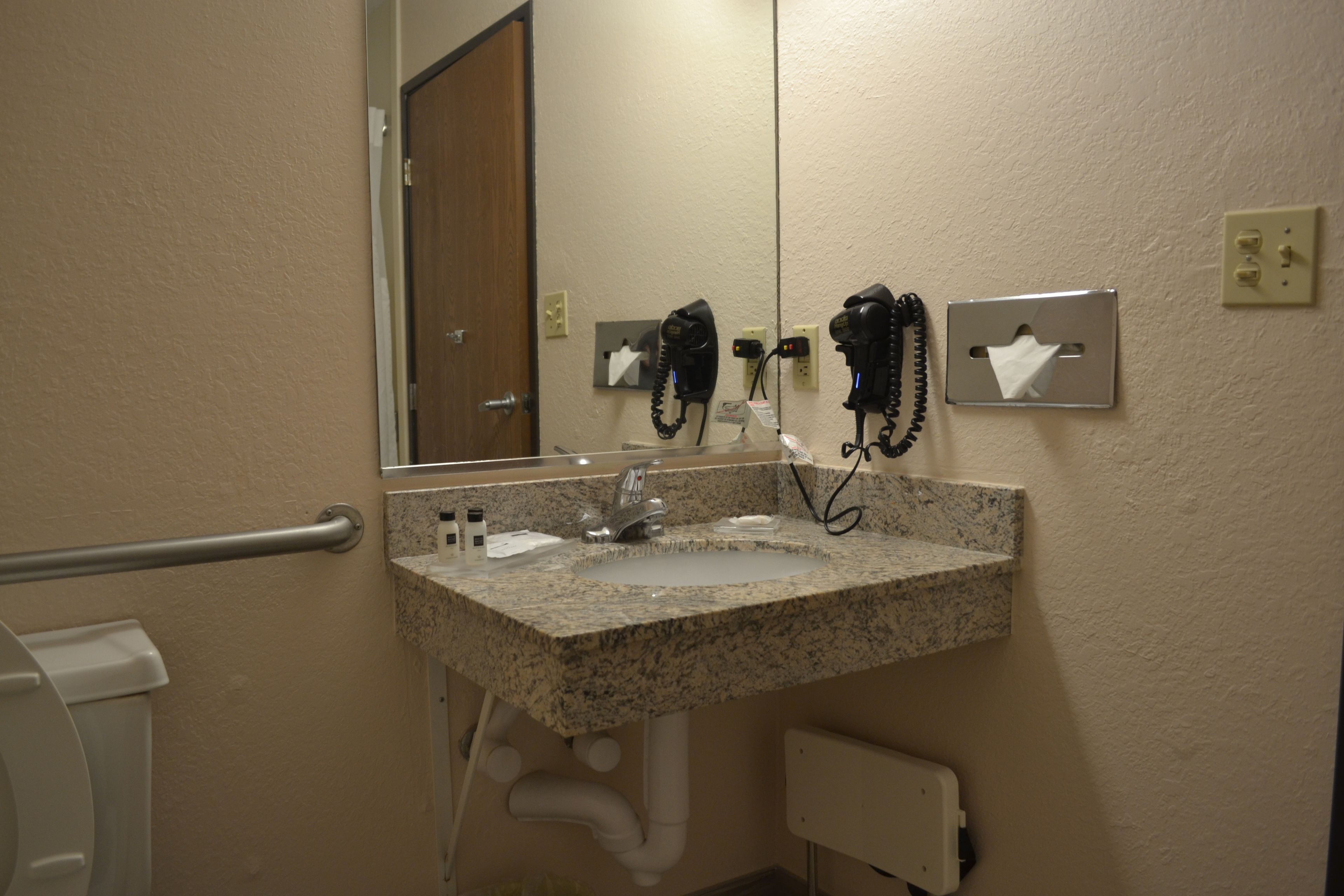 Une salle de bain équipée d’un lavabo en granit, d’un miroir, d’un sèche-cheveux et d’un distributeur de mouchoirs.