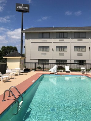 A pool area with clear water, a sign for Country Inn & Suites by Carlson, and a building with multiple windows and a flat roof.