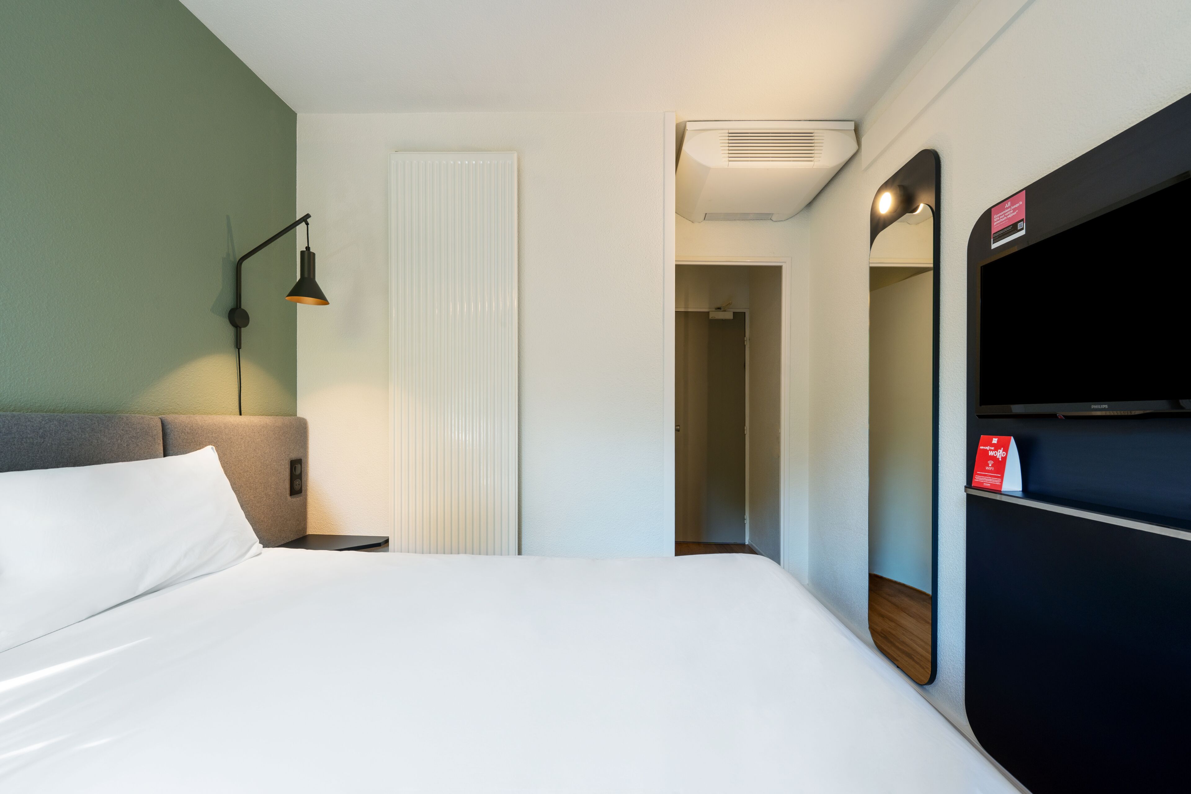 Ein Hotelzimmer mit Bett, Nachttischlampe, Spiegel und Kleiderschrank.