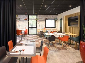 A modern dining area with tables and chairs, a large window, and a projector screen. - ibis Nancy Brabois (Vandœuvre-lès-Nancy)