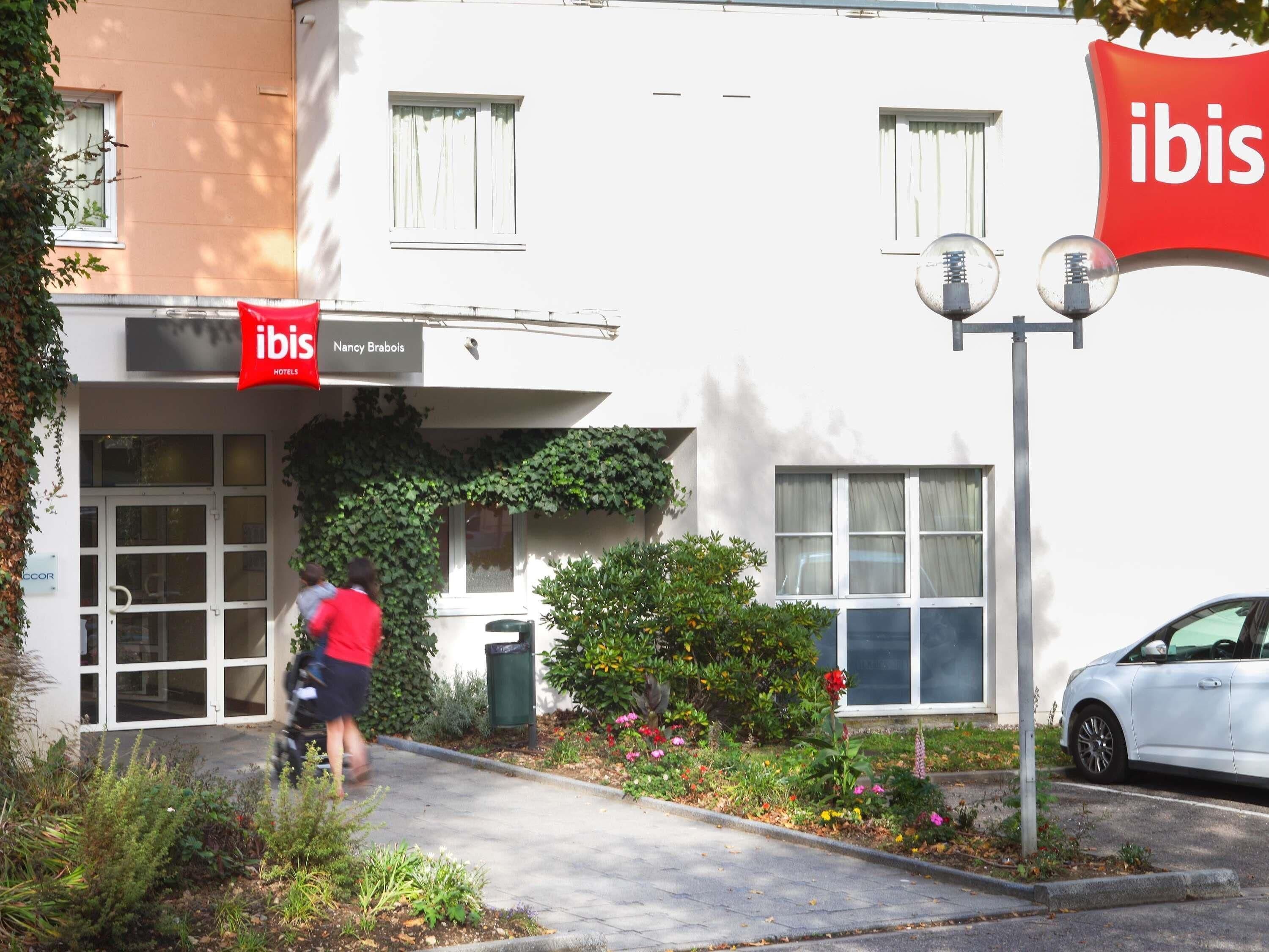 Ein Gebäude mit einem Schild für 'ibis Nancy Brabois Hotels' und einem weißen Auto davor.